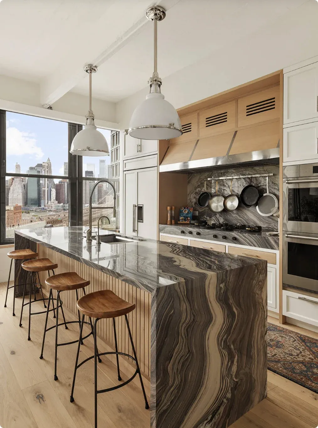A Park Avenue kitchen with a marble waterfall island, brass hardware and a view of the Manhattan skyline
