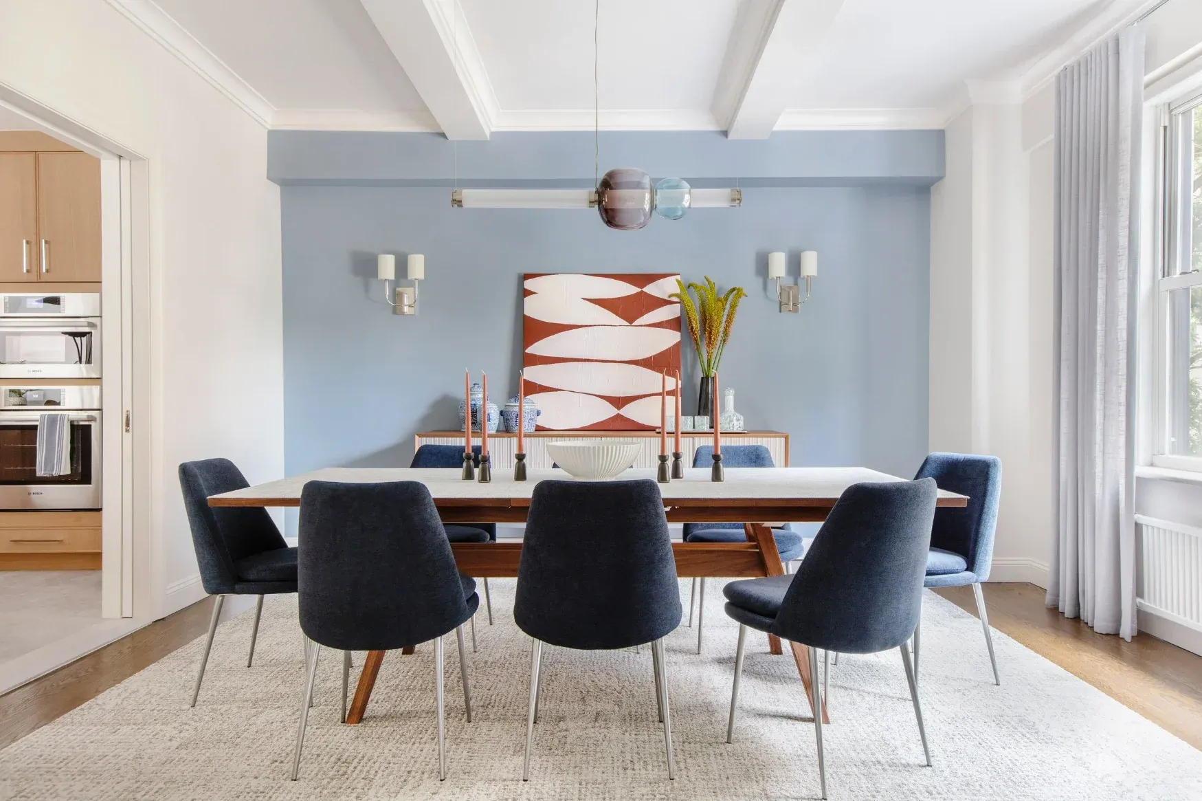 A dining room with a walnut table, navy chairs and a soft blue accent wall
