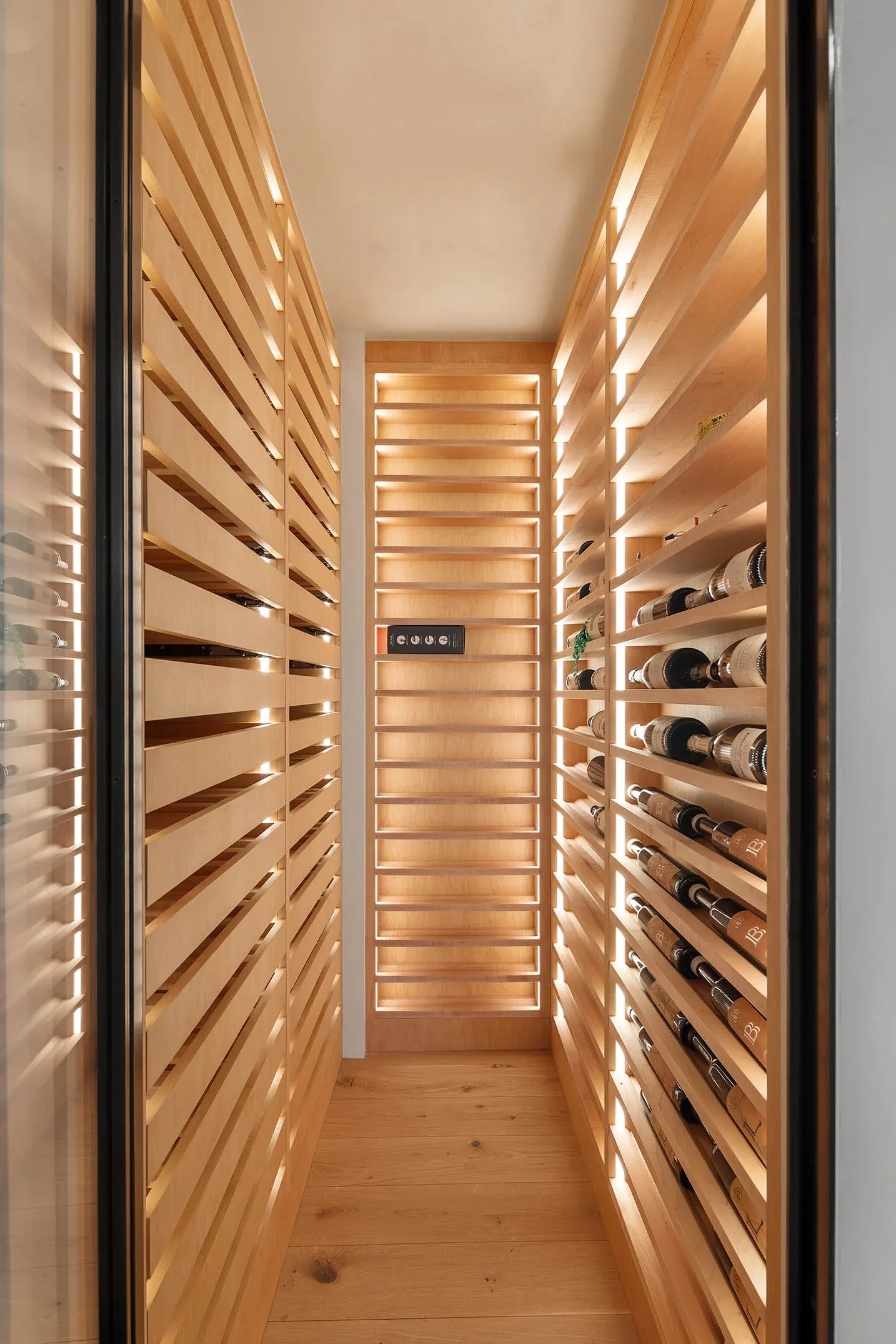 A backlit wine wall with wood slats along a narrow corridor
