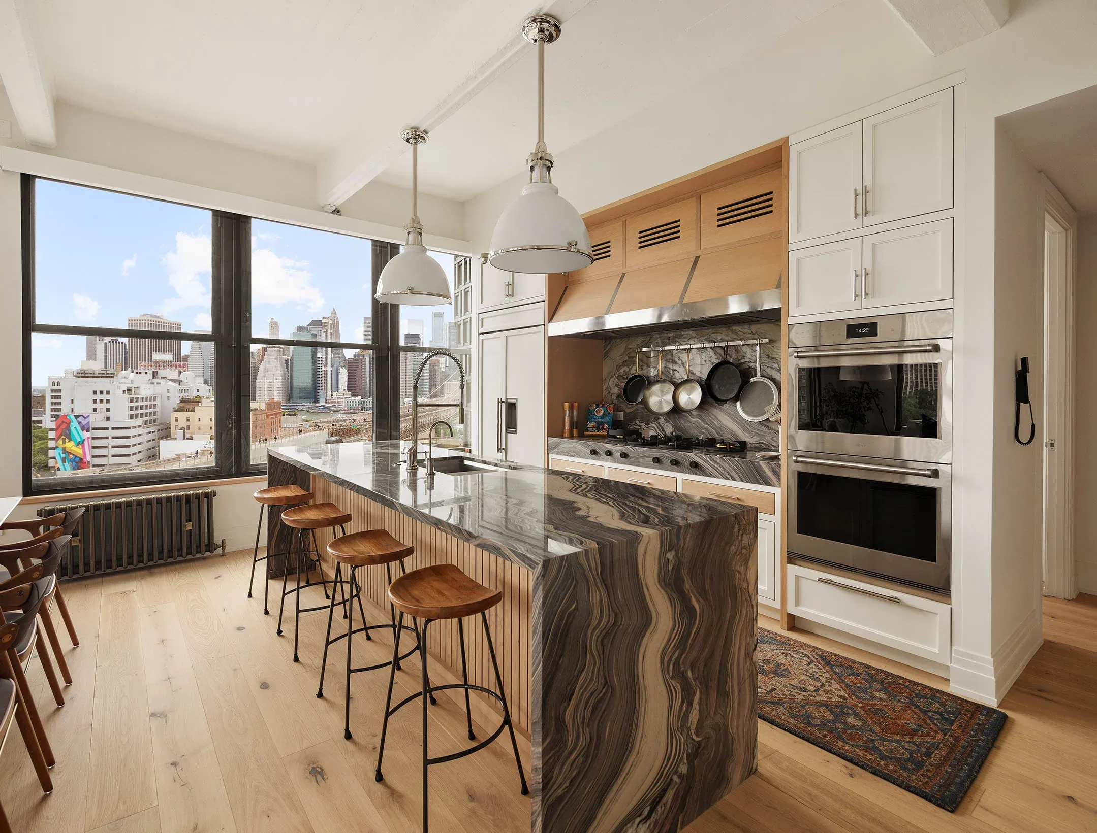 A kitchen with a dramatic veined marble island, leather stools and the Brooklyn skyline outside